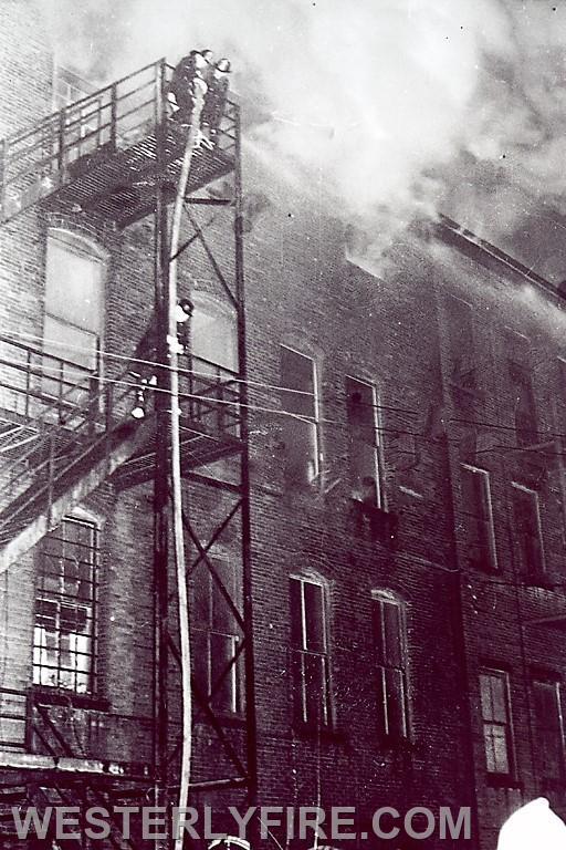 Box 1122-January 8, 1963-Firefighters struggle to stretch a charged 2 1/2 hose line via the rear fire escape to attack the fire in the rear.