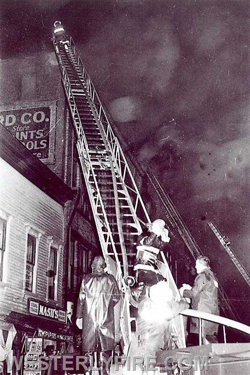 Box 1122-January 8, 1963-Pawcatuck firefighters work using their aerial ladder attempting to knock down the fire in the roof of the Porter-Loveland building.