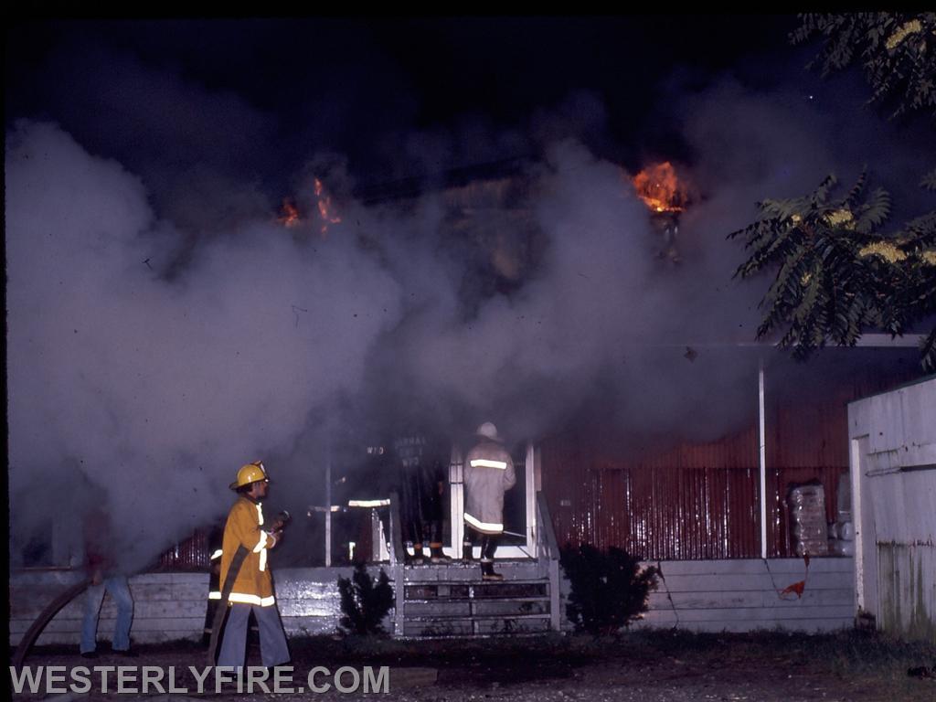 Box 3124-9-14-1975-Firefighters push into the front entrance as the fire still burns overhead.